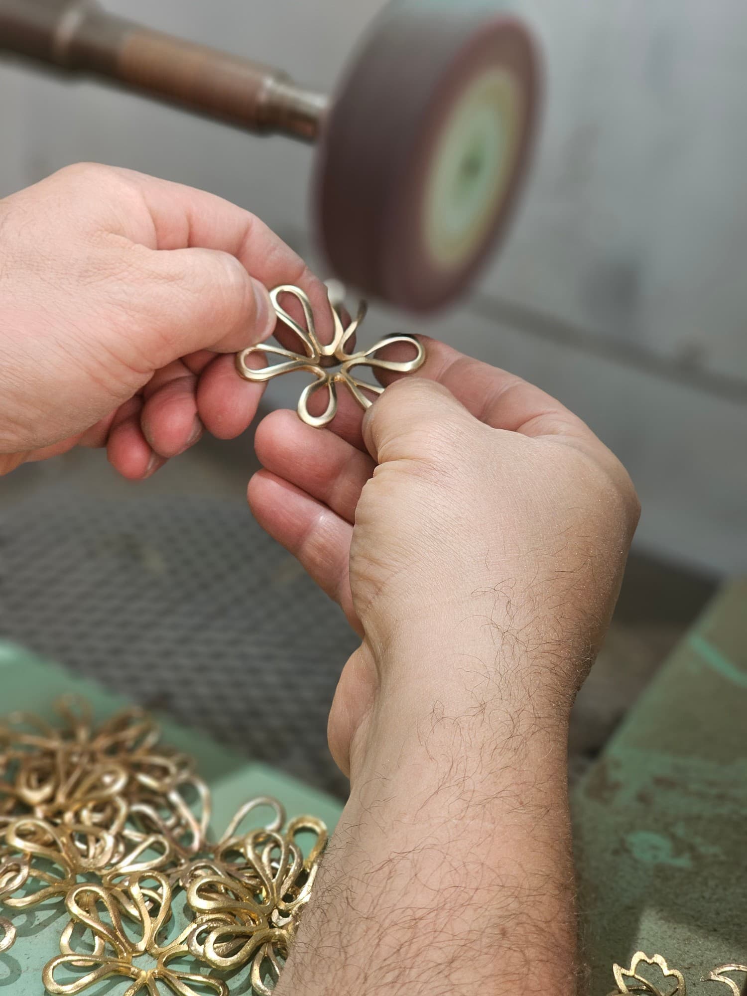 Hands inspecting a gold flower pendant at the polishing wheel